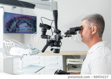 Dentist using dental microscope treating patient teeth at dental clinic office. Medicine, dentistry and health care concept. Dental equipment Dentist using dental microscope treating patient teeth at dental clinic office. Medicine, dentistry and health care concept. Dental equipment 98954227
