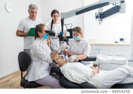 Group of students in dental clinic learn watching dental treatment with a microscope 98954248