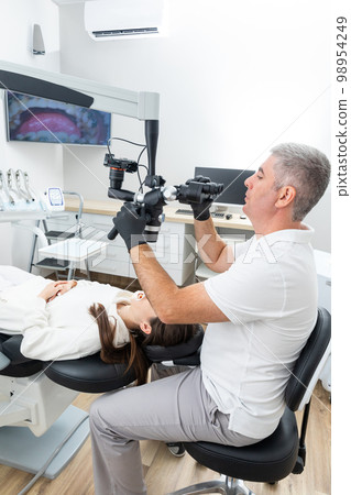 Dentist using dental microscope treating patient with braces in dental office 98954249