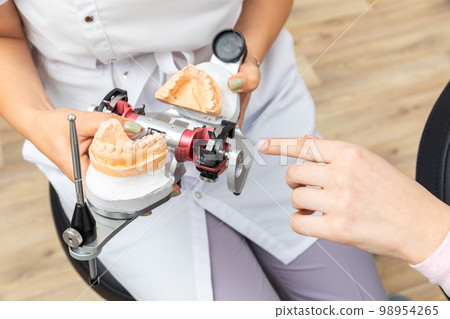 Dentist showing to a client dental articulator with dental gypsum prosthesis model in dental laboratory 98954265