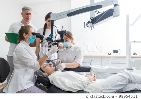 Group of young doctors learning in dental clinic watching dental treatment with microscope 98954511