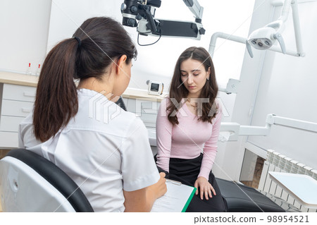 Female dentist filling in papers while talking to young patient in dental office 98954521