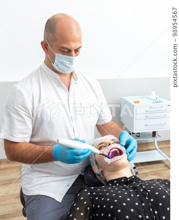 Dentist using dental curing UV lamp on teeth of patient Dentist using dental curing UV lamp on teeth of patient 98954567
