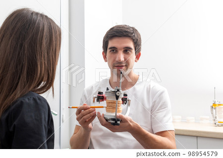 Dentist holding dental articulator with dental gypsum prosthesis model showing it to a patient 98954579
