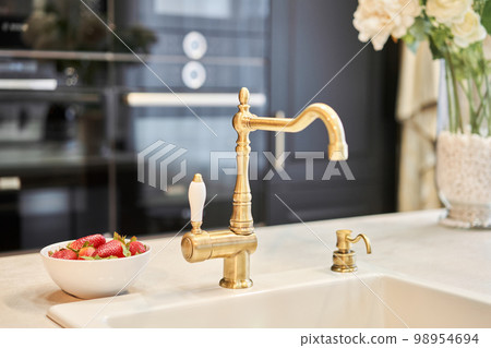 Stylish metallic crane at the kitchen. Sink faucet at the kitchen. Metal crane in close-up photo. Details of the interior of the kitchen in the house. Stylish metallic crane at the kitchen. Sink faucet at the kitchen. Metal crane in close-up photo. Details of the interior of the kitchen in the house. 98954694