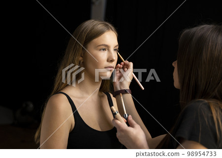 A beautiful young woman with long hair doing makeup for a wedding or photo shoot. Work of a make-up artist. The morning of the bride. Decorative cosmetics. A beautiful young woman with long hair doing makeup for a wedding or photo shoot. Work of a make-up artist. The morning of the bride. Decorative cosmetics. 98954733
