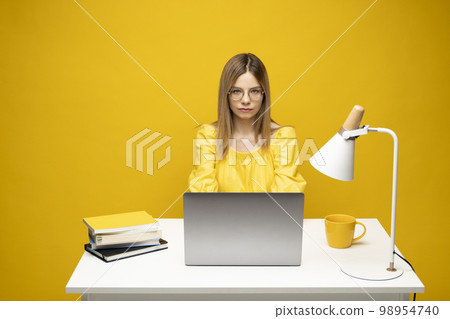 Young blonde freelancer woman in a yellow shirt using laptop for remote work, e-learning at university college, e-banking, online shopping, webinars. Yellow bakcground. Young blonde freelancer woman in a yellow shirt using laptop for remote work, e-learning at university college, e-banking, online shopping, webinars. Yellow bakcground. 98954740