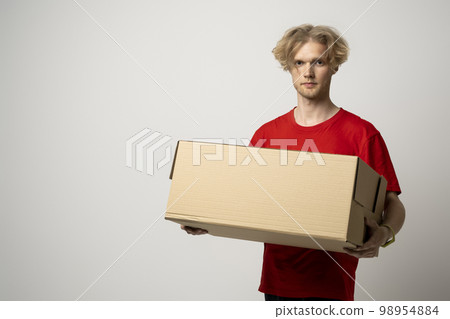 Portrait of a young delivery man, courier in red cap and t-shirt standing with parcel post box isolated over white background. Portrait of a young delivery man, courier in red cap and t-shirt standing with parcel post box isolated over white background. 98954884
