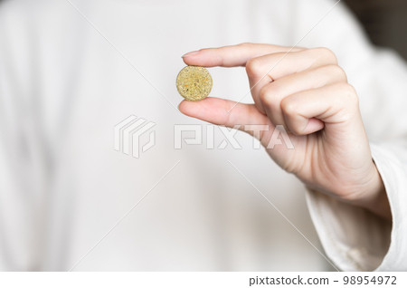 Close-up of a woman holding a pill, a herbal capsule in her hand against the background of a white sweater in blur 98954972