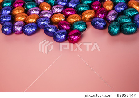 Pile of shiny wrapped chocolate Easter eggs, in colors red, blue and golden,green and purple. Festive Easter concept, top view pink background Happy easter close-up candy sweets concept Pile of shiny wrapped chocolate Easter eggs, in colors red, blue and golden,green and purple. Festive Easter concept, top view pink background Happy easter close-up candy sweets concept 98955447