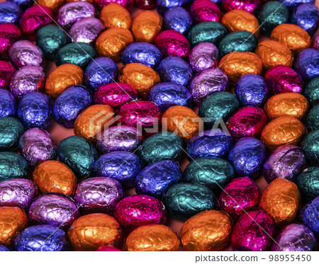 Pile of shiny wrapped chocolate Easter eggs, in colors red, blue and golden,green and purple. Festive Easter concept, top view pink background Happy easter close-up candy sweets concept 98955450