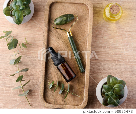 Brown glass bottle with pipette and green stone roller massager on a brown wooden background Brown glass bottle with pipette and green stone roller massager on a brown wooden background 98955478