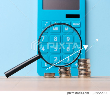 A stack of metal coins and a plastic magnifier on a blue background. The concept of increasing taxes, subsidies A stack of metal coins and a plastic magnifier on a blue background. The concept of increasing taxes, subsidies 98955485
