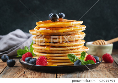 Delicious pancakes, with fresh blueberries, raspberry and maple syrup or honey on a dark background Delicious pancakes, with fresh blueberries, raspberry and maple syrup or honey on a dark background 98955794