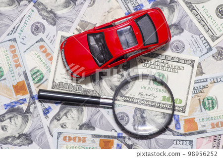 Magnifying glass and toy red car on dollar bills background Magnifying glass and toy red car on dollar bills background 98956252