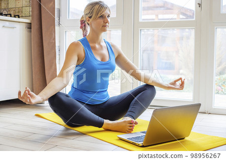 Young sporty woman in sportswear practicing meditation with laptop at home 98956267