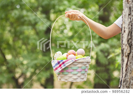 Child hand holding basket full of colorful easter eggs after egg hunt Child hand holding basket full of colorful easter eggs after egg hunt 98956282