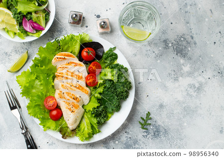 Chicken breast fillet and vegetable salad with tomatoes and green leaves on a light background. The concept of healthy food and keto diet. Top view with copy space 98956340