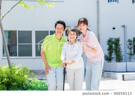 A senior woman and her caregiver taking a walk outdoors with a cane Cooperation: Chuo College of Technology Japanese Language School 98956513