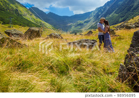 young couple sitting on a rock in front of high mountains 98956895