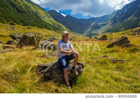 man in straw hat sits on a rock against the background of high mountains man in straw hat sits on a rock against the background of high mountains 98956900