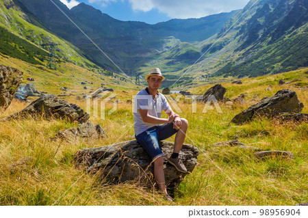 man in straw hat sits on a rock against the background of high mountains 98956904