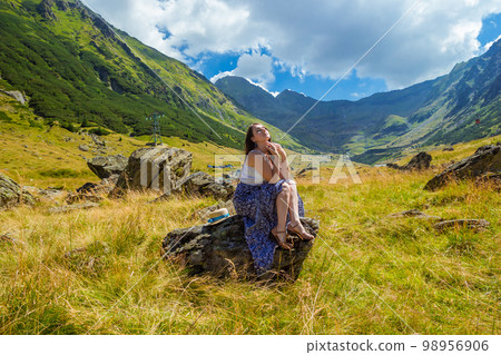 girl in long blue dress sits on a rock in the mountains 98956906