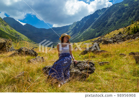 girl in dress and hat sits on a rock against the background of high mountains 98956908