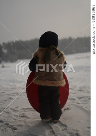 A lonely child in a snowy field from behind 98956965