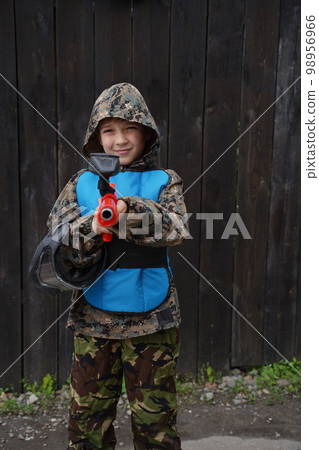 Cheerful positive boy paintball player in camouflage standing with gun before playing outdoors. 98956966