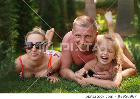 Young family with children having fun in nature. Cheerful family lies in swimsuits on the grass. Parents and daughter laugh on vacation in the summer. Selective focus 98956967