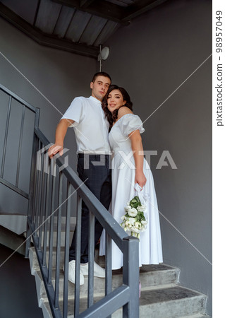 Bride and groom stand on the stairs, portrait of the newlyweds, a bride with a bouquet of white flowers. Valentine's Day 98957049