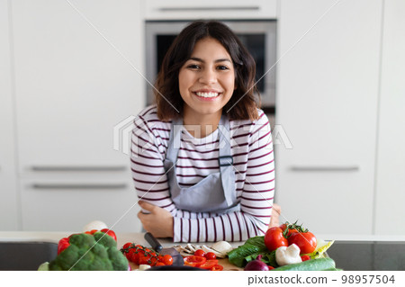 Portrait of happy beautiful young hispanic woman posing in kitchen Portrait of happy beautiful young hispanic woman posing in kitchen 98957504