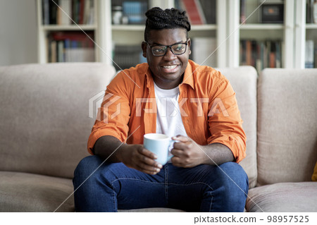 Relaxed african american chubby guy drinking tea at home 98957525