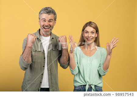 Wow, yes. Overjoyed middle aged spouses cheering and shaking clenched fists, looking at camera in excitement 98957543