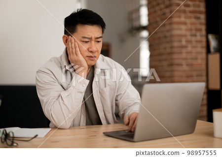 Sad middle aged man employee working on laptop at home office, looking at computer screen, copy space 98957555