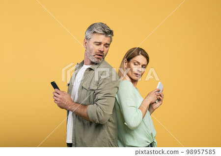 Privacy concept. Middle aged caucasian man trying to look at his wife's smartphone, woman hiding screen of her gadget Privacy concept. Middle aged caucasian man trying to look at his wife's smartphone, woman hiding screen of her gadget 98957585