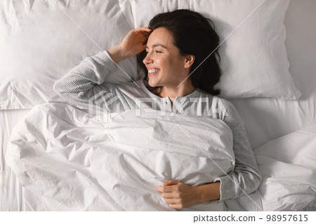 Cheerful pretty young european lady sleeping on white bed, waking up, enjoying good morning, vacation 98957615