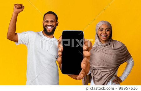 Overjoyed black muslim couple showing big blank smartphone with empty screen Overjoyed black muslim couple showing big blank smartphone with empty screen 98957616