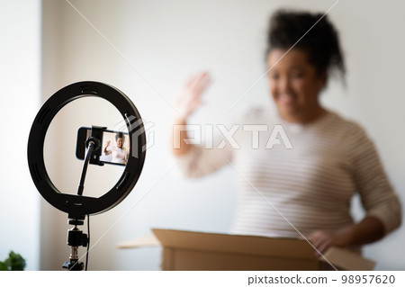 Cheerful overweight lady streaming while opening delivery. Blogging concept 98957620