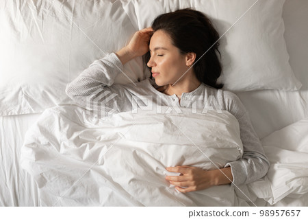 Smiling calm caucasian millennial lady sleeps on comfortable bed, enjoys weekend, vacation and spare time 98957657