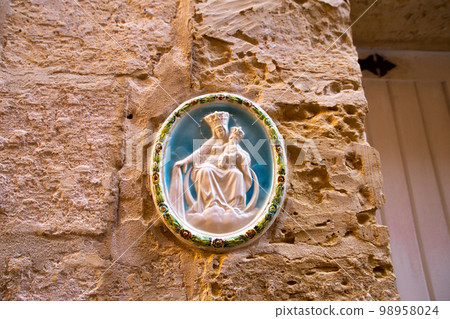 Traditional religious catholic bas-relief od Virgin Mary with baby Jesus near the building entrance in Mdina, Malta. Traditional religious catholic bas-relief od Virgin Mary with baby Jesus near the building entrance in Mdina, Malta. 98958024