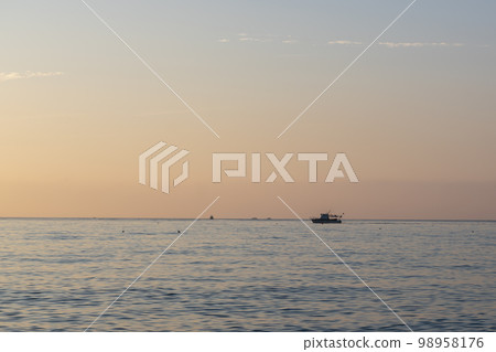 Evening sunset over the sea with a sea boat sailing on the horizon. Evening sunset over the sea with a sea boat sailing on the horizon. 98958176