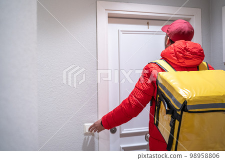 Food delivery man courier at a house door rings the bell. Food and drink delivery concept.  98958806