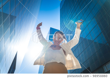 Happy businesswoman celebrating good news in front of business buildings. Happy businesswoman celebrating good news in front of business buildings. 98958860