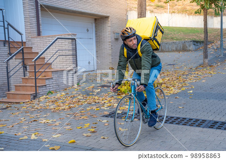 Delivery man riding bike delivering food and drink in town outdoors on stylish bicycle and backpack. 98958863