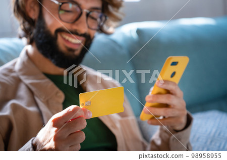 Happy Caucasian man buying things online, using smartphone and credit card, shopping in internet 98958955