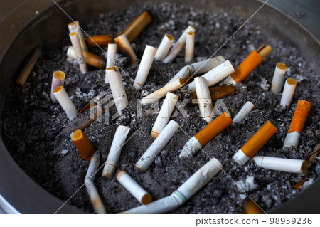 Cigarettes and ash on dirty sand in trash tray 98959236