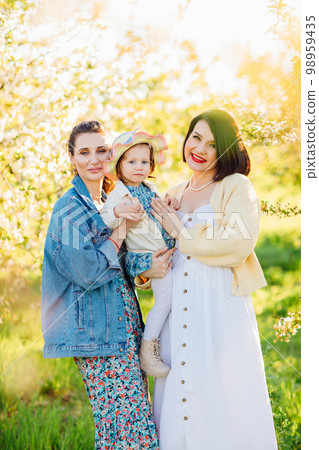 two attractive women with a little girl in their hands in a spring garden.  98959435
