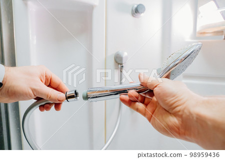 men's hands screw the shower head onto a new hose. men's hands screw the shower head onto a new hose. 98959436